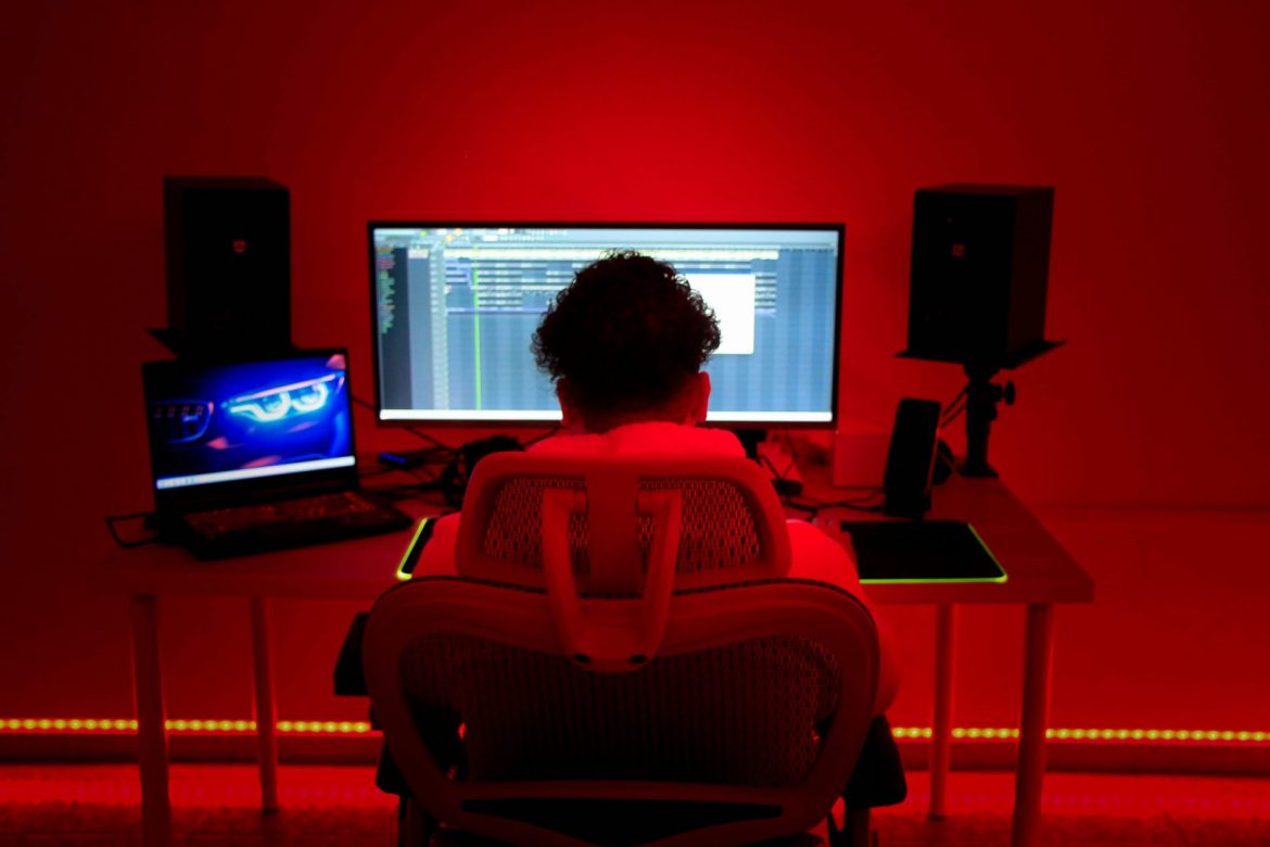Mann sitzt vor einem Bildschrim und Laptop in einem Homestudio mit roter Beleuchtung